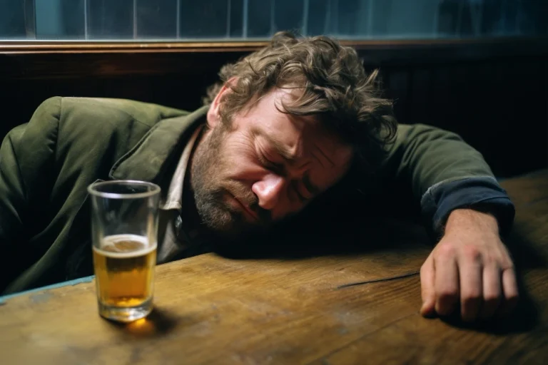 Mężczyzna śpiący przy stole obok piwa w szklance