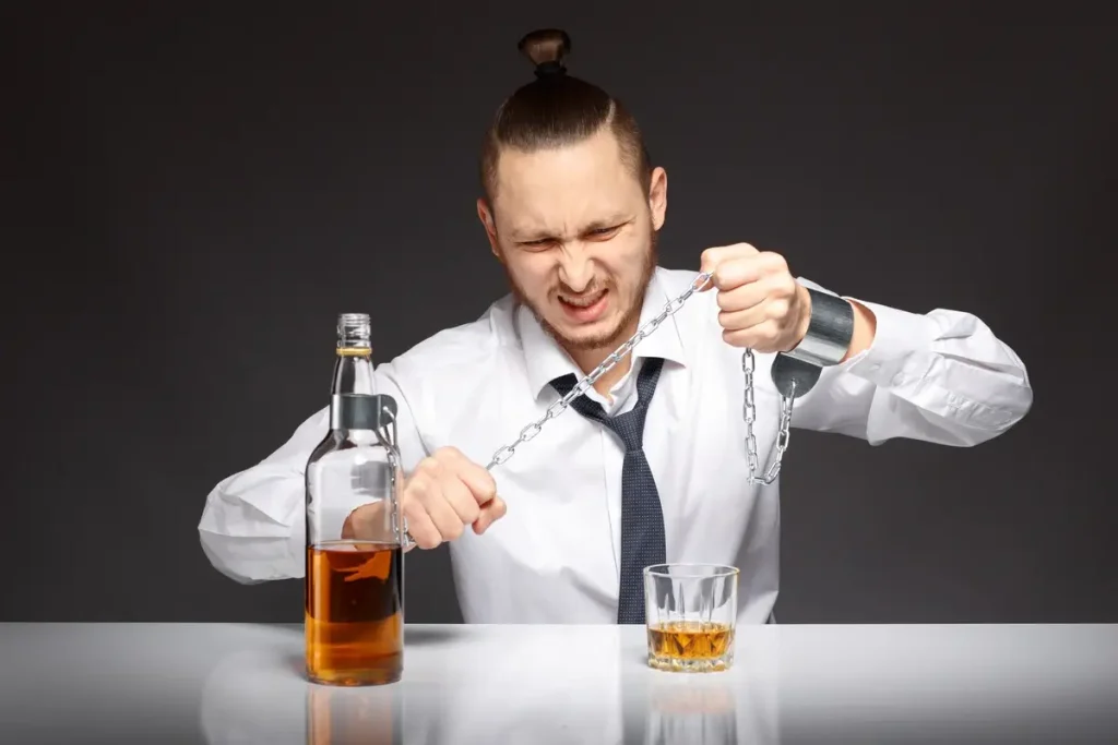 Mężczyzna uwiązany łańcuchem do butelki alkoholu symbolizujący zniewolenie przez nałóg